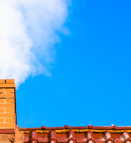 Modern house roof with chimney smoke, air pollution and smog in winter